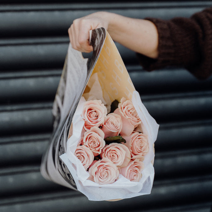 Bouquet of pink roses wrapped in newspaper held by a person against a dark background
