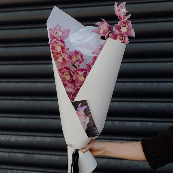 Bouquet of pink flowers wrapped in white paper with a black background