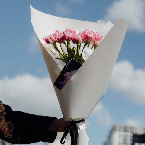 Bouquet of pink tulips wrapped in white paper against a blue sky with clouds.
