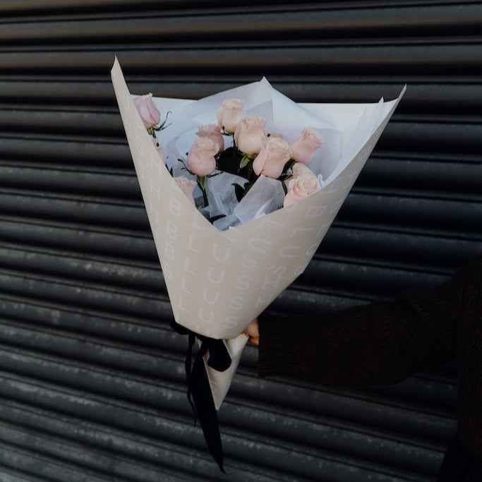 Bouquet of flowers wrapped in white paper with a black ribbon against a dark background